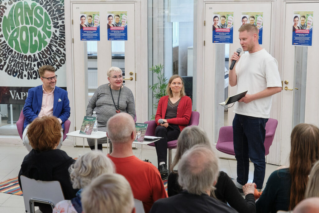 Paneelikeskustelijat ja moderaattori hymyilevät yleisön edessä.
